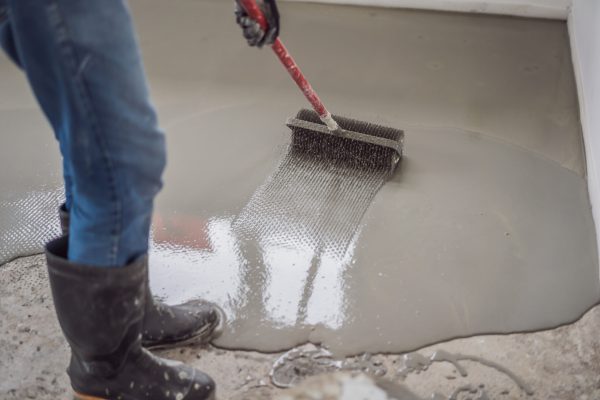 plasterer during floor covering works with self-levelling cement mortar, uses a needle roller.